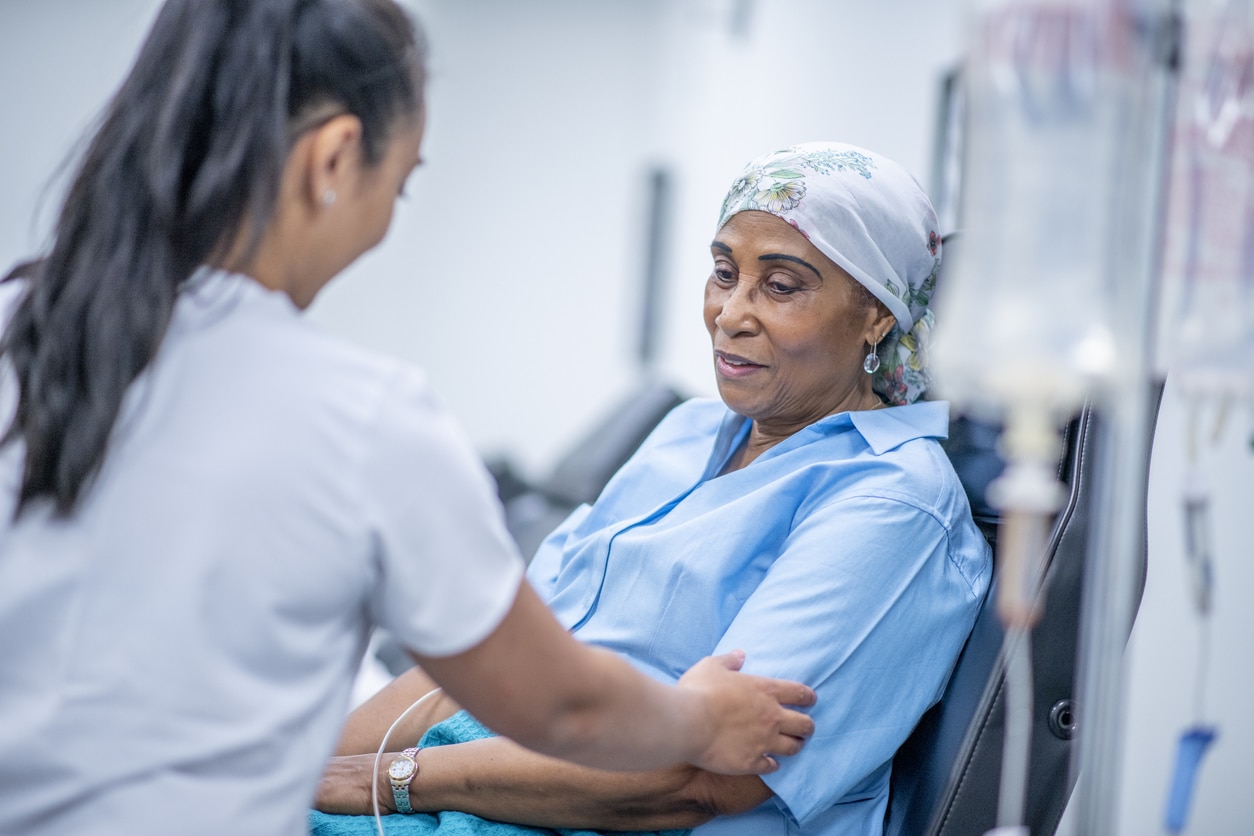 A woman wearing a head scarf recovers from chemo treatment in the hospital. A doctor speaks with her and offers her support.