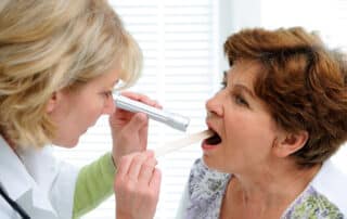 In a clinical setting, a woman doctor examines the mouth of a woman patient, who is suffering from xerostomia - often called "dry mouth."