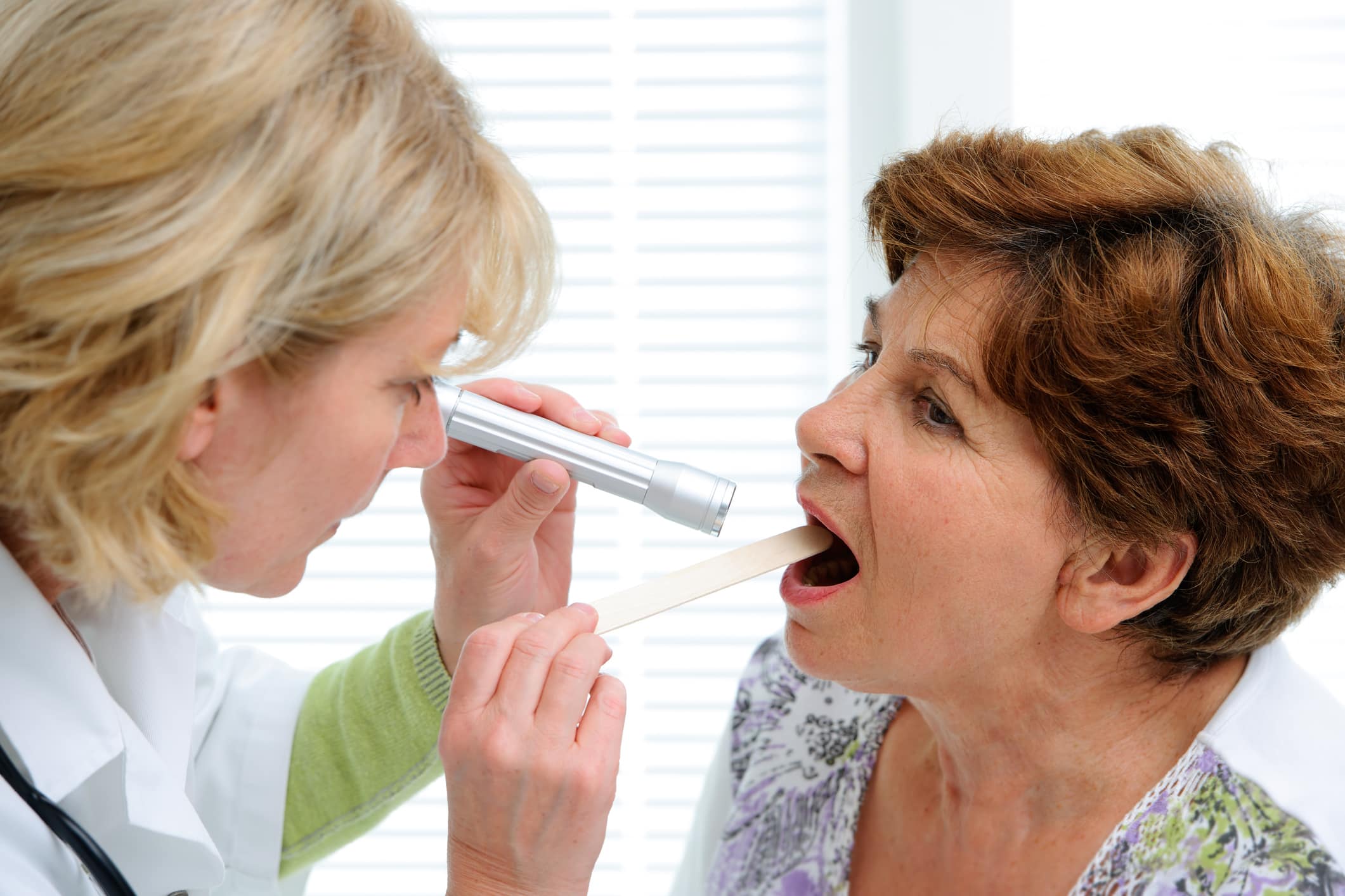 In a clinical setting, a woman doctor examines the mouth of a woman patient, who is suffering from xerostomia - often called "dry mouth."