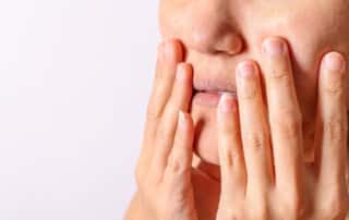 A woman, possibly suffering from xerostomia - commonly known as dry mouth - touches her face with her hands in discomfort.